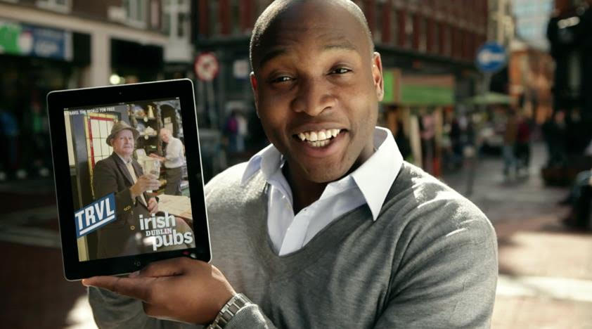 The photo is an advertisement for TRVL magazine. It depicts a male model holding an iPad with a TRVL magazine photo on it promoting a story on pubs in Dublin, Ireland.